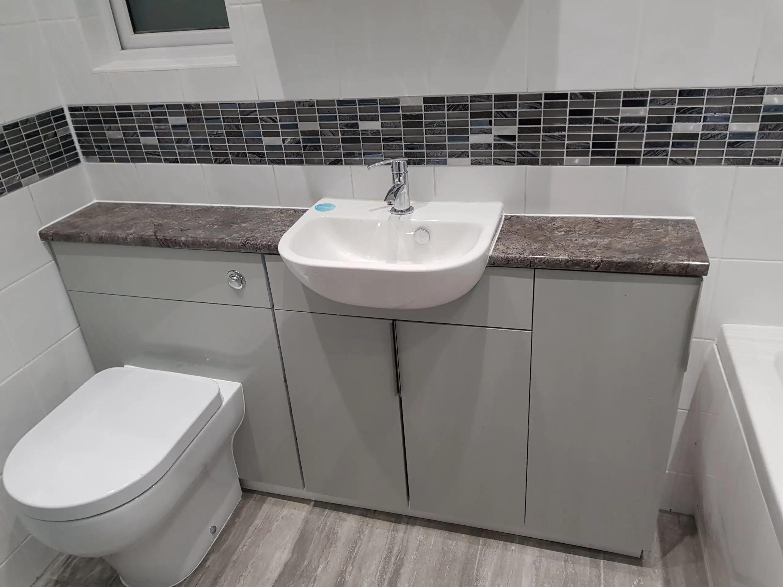 Bathroom vanity unit with a sink and a mosaic tile border above white wall tile